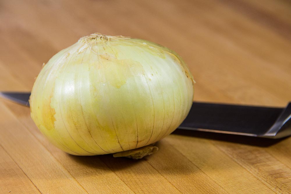 Whole Sweet Onion on Wooden Cutting Board Near Chef's Knife