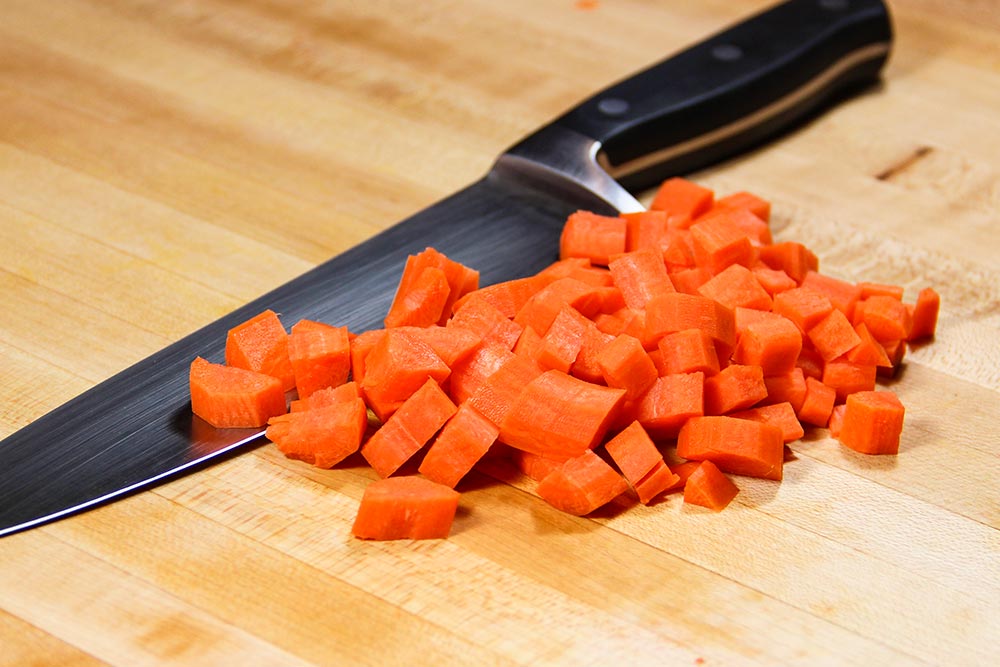 Diced Carrot With Chefs Knife on Wooden Cutting Board